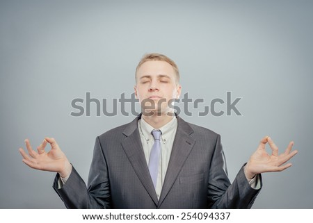 Young businessman meditating, isolated grey wall background. Stress relief techniques at work concept. Take a deep breath.nd. Stress relief techniques at work concept. Take a deep breath.