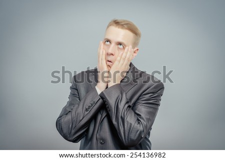Portrait of young desperate businessman pulling his face down isolated on gray background