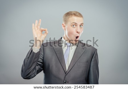 Everything is OK! Happy young man in suit and tie gesturing OK sign and smiling while standing against grey background