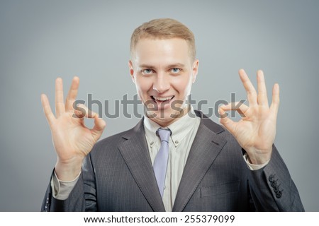 Gesturing OK sign. Cheerful young man in shirt and tie gesturing OK sign while standing against grey background