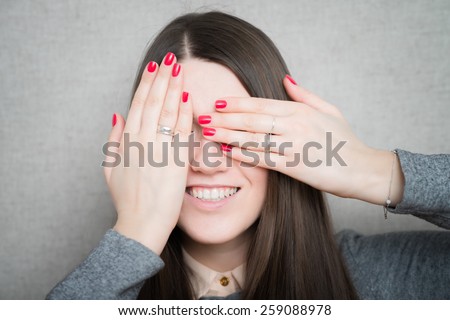 smiley woman covering her eyes by hands over dark background