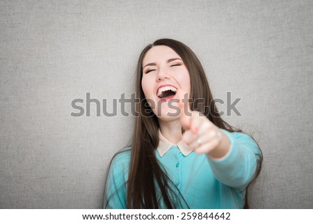 portrait of attractive smile laugh teenage girl, pointing her finger, wear green shirt, white teeth, brown long hair, isolated over white background concept of student point at you, young pretty woman
