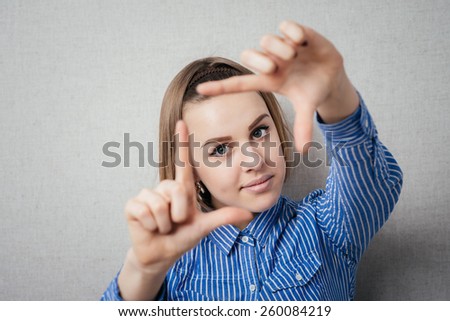 Gesturing finger frame. Beautiful young woman looking at camera and gesturing finger frame while standing against grey background