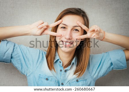 Young woman watching through fingers victory glasses over a grey background