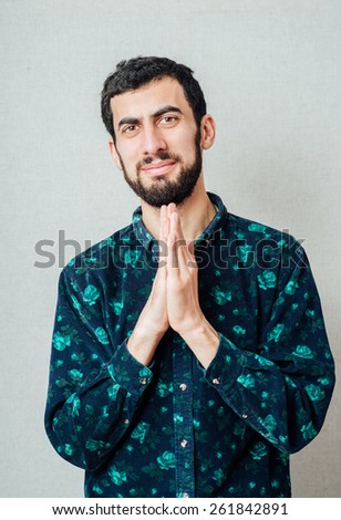 Young handsome man praying hands near your mouth. Gesture. On a gray background