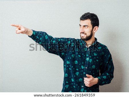Handsome bearded Caucasian man in blue  shirt smiles and points with finger