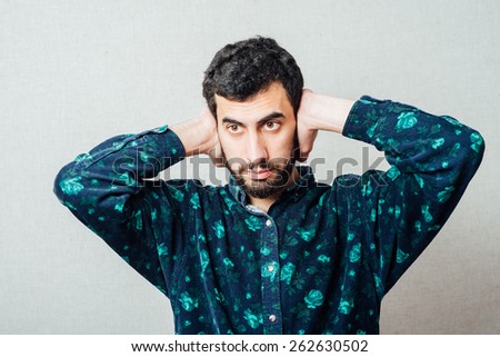 Closeup portrait of a young handsome beard man in shirt holding hands to ears covering to shut out noise looking  at neighbors
