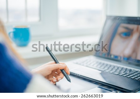 Young graphic designer working on laptop using tablet at home.