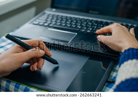 Young graphic designer working on laptop using tablet at home.