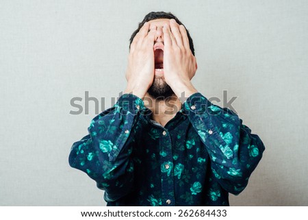 Unleashed emotions. Furious young bearded man shouting while standing against grey background