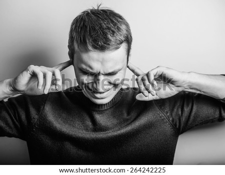 Blond young man shows he does not want to hear from you. Fingers in his ears. gesture. Close portrait.