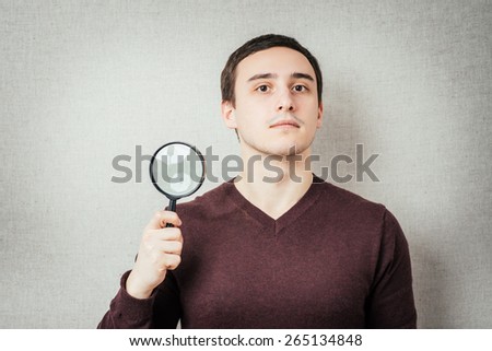 Man with magnifying lens over grey background. / Portrait of a normal man looking camera.