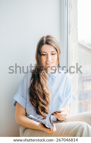 Attractive girl reading magazine on  window. girl holding magazine at home