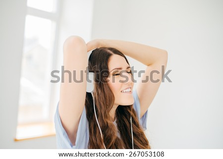Happy girl dancing at home while listen music with headphones. She is in her house in front of the big window in nature view