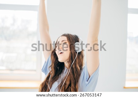 Happy girl dancing at home while listen music with headphones. She is in her house in front of the big window in nature view