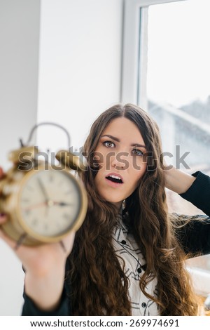 Closeup portrait woman extending hand to alarm clock. Human face expression, emotion, feeling.