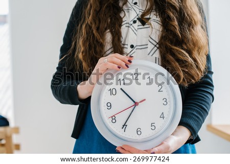 Confident Friendly Young Caucasian  Woman Holding A Large Clock In Hands Showing The Success And Joy Of Good Office Timekeeping In A Happy Hour Concept