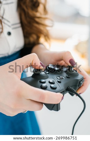 Attractive young woman with long curly brunette hair on a background window playing computer game at home.