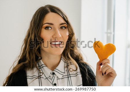 portrait of attractive  caucasian smiling woman with long curly hear brunette with yellow heart in hands near the window
