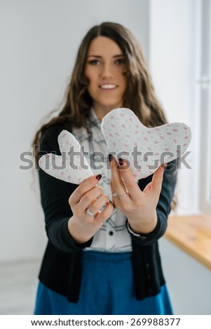 Picture of 2 small white hearts in hands, female holds handmade sewn soft toy, woman with Valentine gift against the window, happy girl smiling, conceptual image of health care or love.