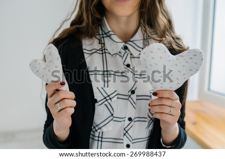 Picture of 2 small white hearts in hands, female holds handmade sewn soft toy, woman with Valentine gift against the window, happy girl smiling, conceptual image of health care or love.