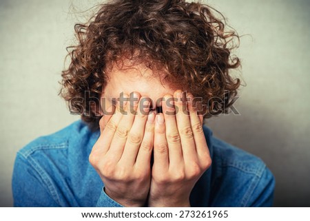 Curly young man crying, sad, covered his face with his hands. On a gray background