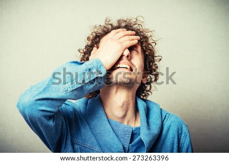 Curly young man crying, sad, covered his face with his hand. On a gray background
