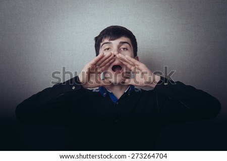 A man shouts with his hands around his mouth. Gesture cry, cry, search a person or an animal or other. On a gray background