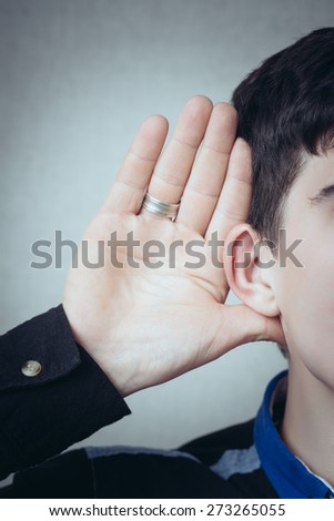 A man with his hand near his ear. Gesture can not hear without listening, talking louder. On a gray background