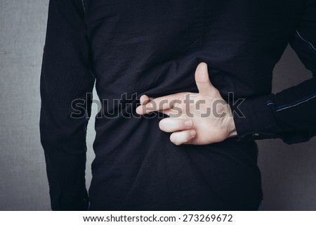 Male hands behind his back, fingers crossed. Luck, the desire to think. Gesture. On a gray background.