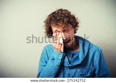 Curly man crying with a handkerchief wiping tears from her eyes. On a gray background.