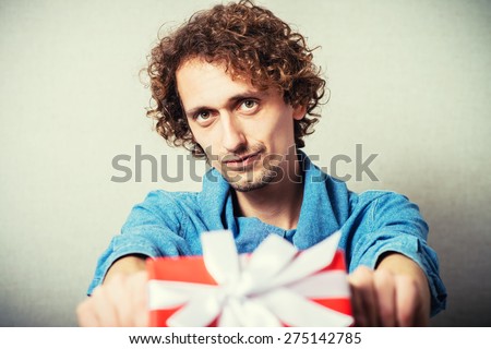 Curly man gives a gift, red box with white bow. On a gray background.