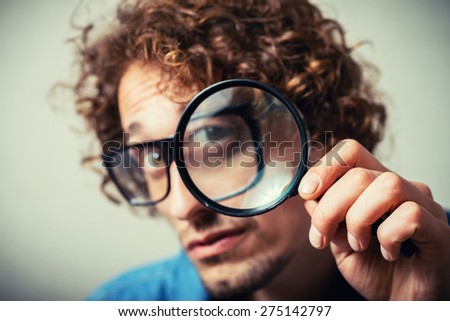 Curly man looking through a magnifying glass. On a gray background.