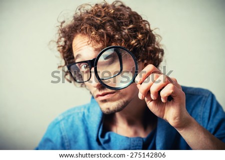 Curly man looking through a magnifying glass. On a gray background.