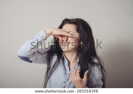 The woman closed nose with her hand, a bad smell. On a gray background.