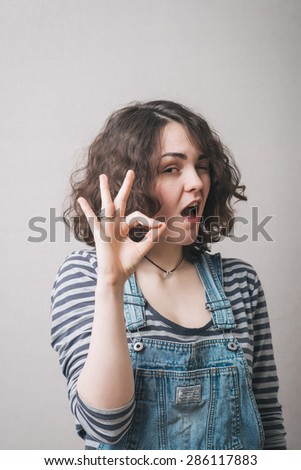 Young cute smiling girl showing OK sign on gray