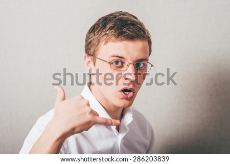 The man in glasses makes a gesture call me. On a gray background.
