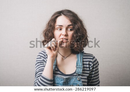 The woman lost in thought, chewing on nails from experiences fear. On a gray background.