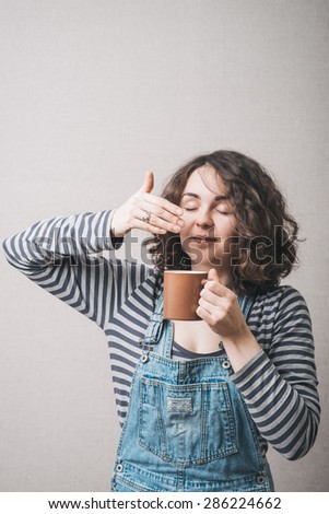 The woman inhales the smell of a cup of coffee or tea. Gray background
