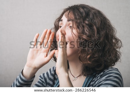 A woman makes a gesture calling someone with hands near your mouth. Gray background