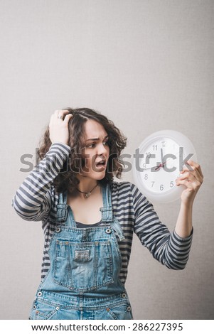 A woman looks at the big clock and holding his head, is late. Gray background