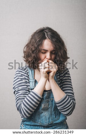 Sad woman looking down holding fists near his mouth. Gray background