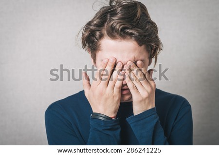 The man was crying, very upset, he covered his face with his hands. Gray background