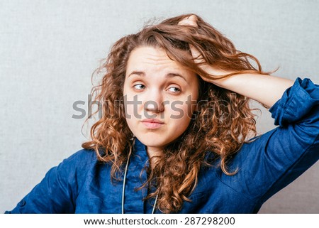 Curly woman scratching her head. Gray background.