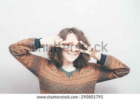Curly girl shows a gesture of victory, near the eyes.
