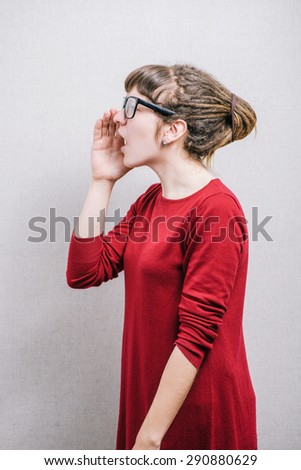 Woman in glasses calling with a hand to her mouth, profile. On a gray background.