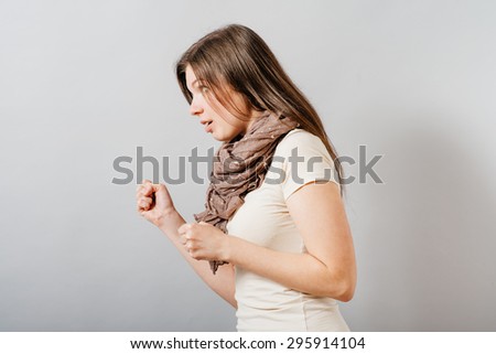 Young woman with angry fists profile. On a gray background.