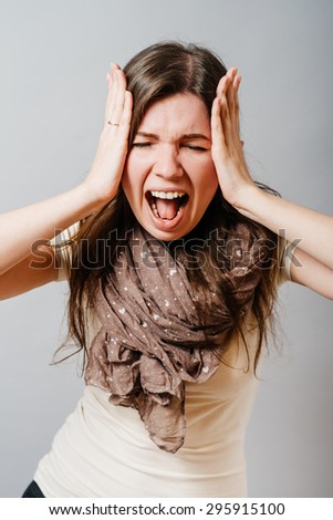Young woman screaming with hands over head. On a gray background.
