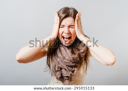 Young woman screaming with hands over head. On a gray background.