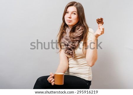 Young woman sitting on a chair with a cup and cookies. On a gray background.